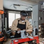 Man Wearing Checkered Long Sleeves and an Apron in a Workshop working on a lathe